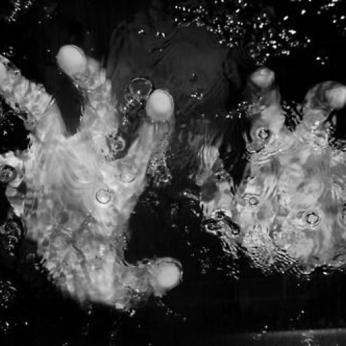 A pair of hands are underwater reaching out to the viewer