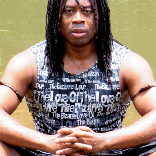 Anani Dodji Sanouvi sitting in a body of still water in a black tank top with brown bands on his upper arms