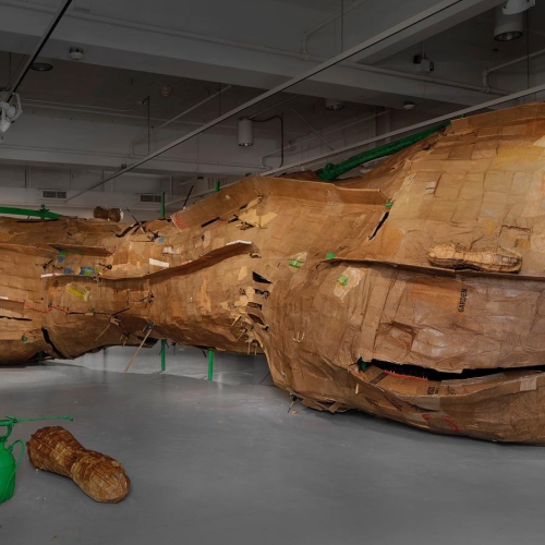 A large brown wooden abstract sculpture that resembles a rock formation with rounded edges