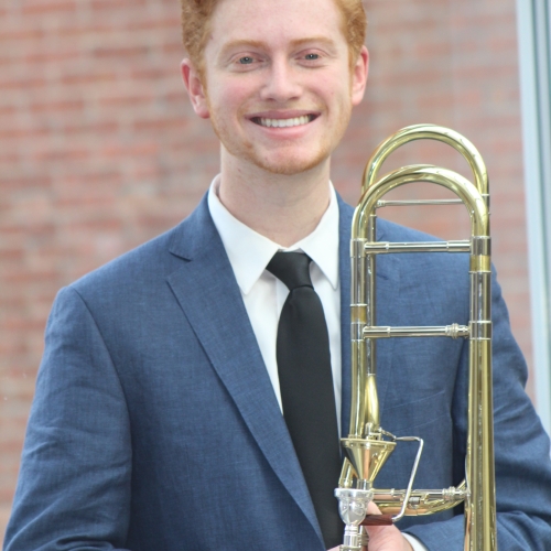 A redhead holds a trombone and smiles