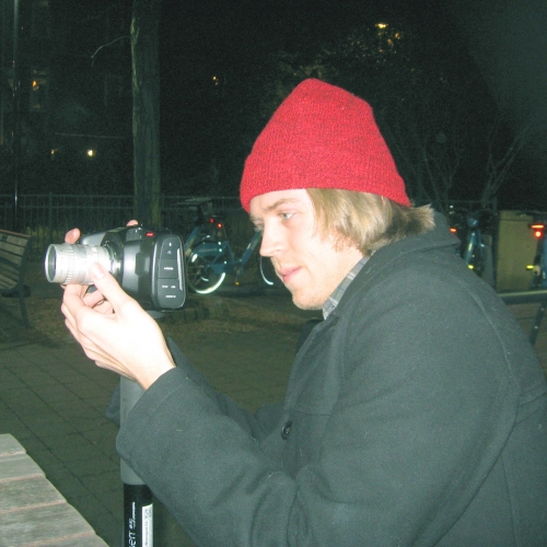 A boy in a red beanie looks through a camera lens. 