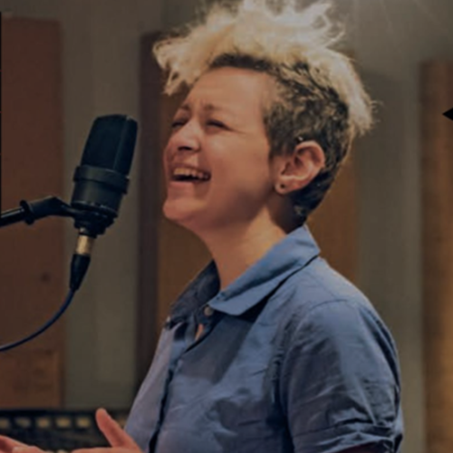 Farah Cuckor singing into mic in studio, blonde hair, blue collared shirt
