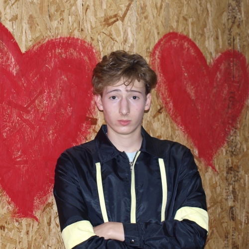 A photo of Isaac Finn in front of plywood with two red hearts painted on it.