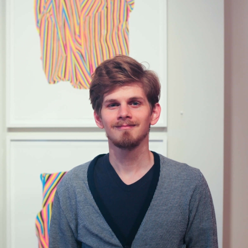 justin rubich headshot wearing cardigan and against the background of a painting