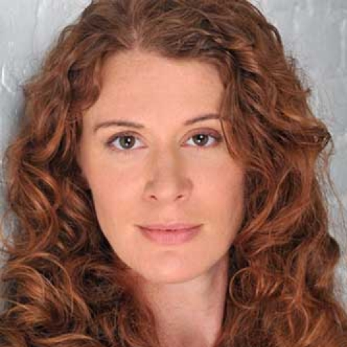 A headshot of Krista Apple, wearing a black shirt and against a gray, textured background.