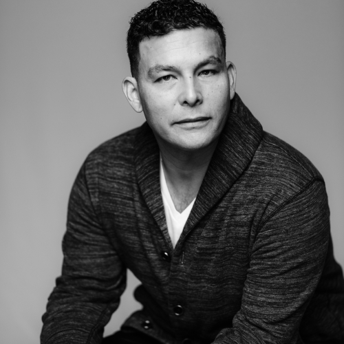 A black and white portrait of Meshi Chavez in a cardigan and a white tee shirt against a gray background