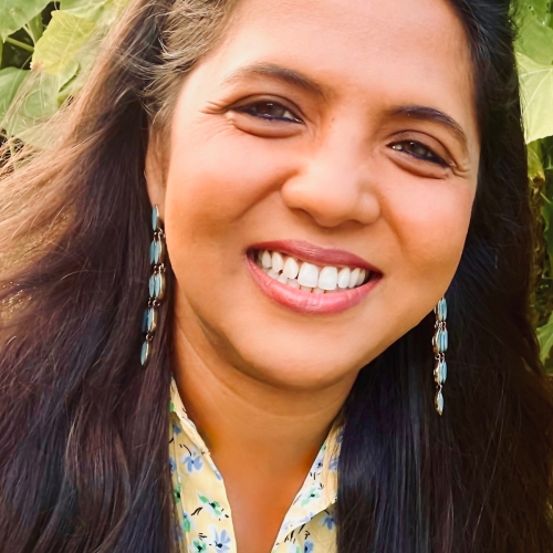 headshot of Priyanjali Sen, seen against a background of leabes and wearing a yellow shirt dotted with small blue flowers