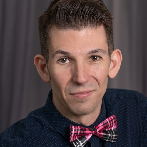 Stearn Matthews in front of a gray curtain and dressed in a navy dress shirt and a pink and black and white bow tie