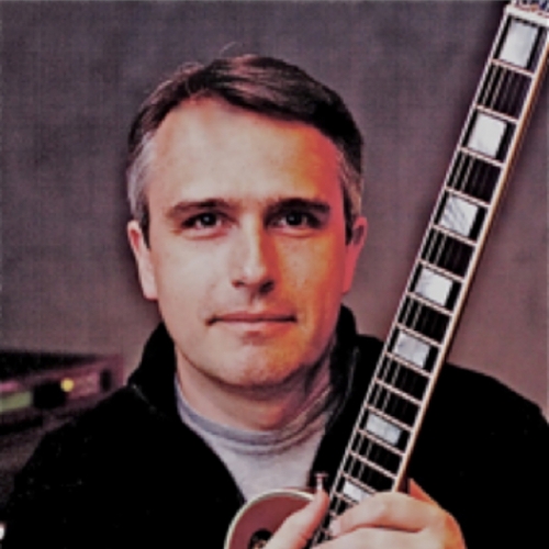 A photo of Tom Hedden holding a guitar.