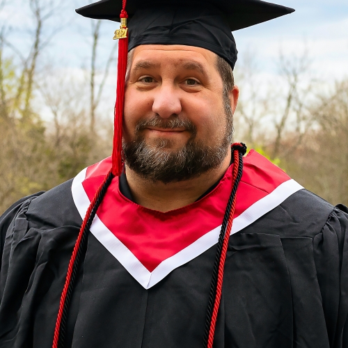 A man smiles wearing graduation cap and gown
