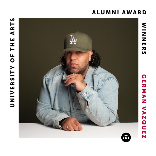 a square labelled image commemorate alumni award winner german vazquez. vazquez is pictured seated leaning on a white counter wearing a pale denim jacket and an olive LA dodgers cap which matches the hue of the blank background. 