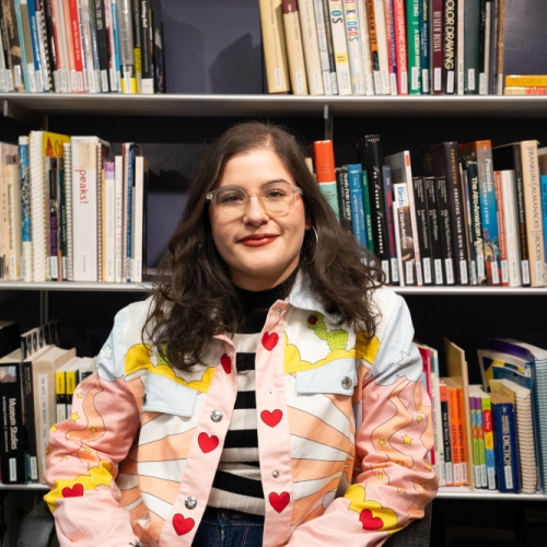 arianna olivieri wearing a pink sunrise and heart patterned jacket against a background of library books