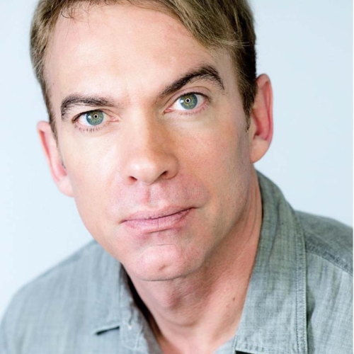 Dave Barrus in a light gray and dark gray plaid shirt in front of a light gray brackground