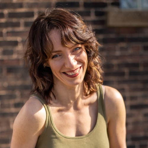 Elizabeth Pollert dressed in a green tank top and standing in front of a brick wall