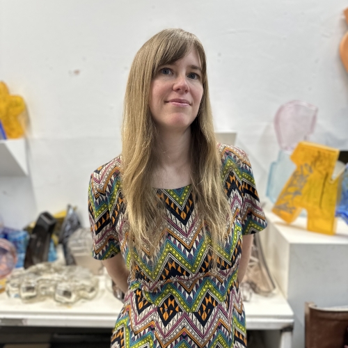 Heather Moqtaderi standing in a studio space in front of yellow and blue and other works on a white table
