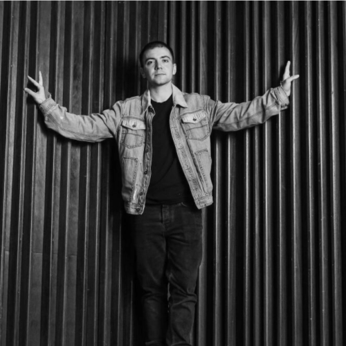 Yves Laris Cohen standing in front of a curtain with their arms outstretched in black and white