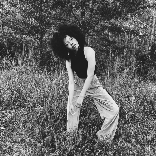 Raven Nishae Leak standing in a partially wooded area and posing in a purposefully limp way in black and white