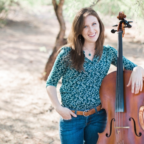 Melissa Brun standing in a wooded clearing and holding her cello