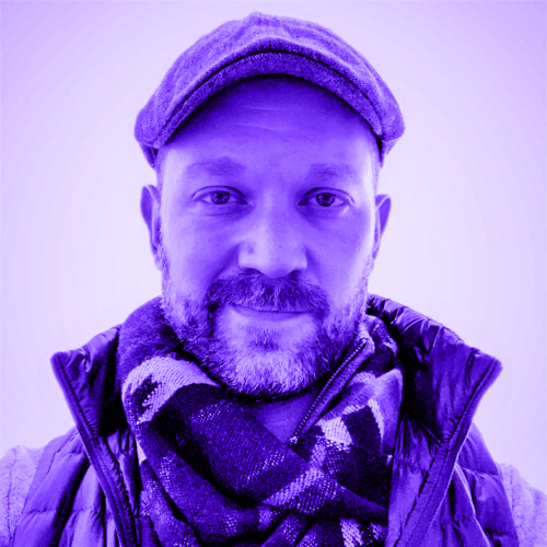 jordan rockford overlaid with a violet hue. jordan is wearing a jacket with a long collar and a large scarf and a flat cap, looking at the viewer with a slight smirk and a beardy face. 