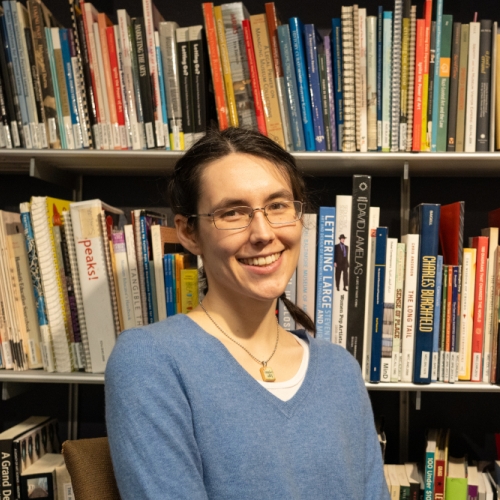 headshot of Sarah Lennox in a blue sweater against a background of library shelving