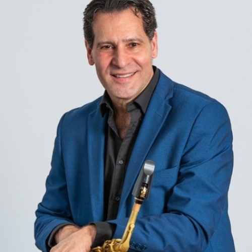Tony Salicandro wearing a blue suit jacket and a black shirt and holding a saxophone in front of a white background