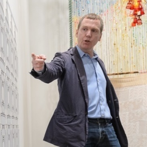 Dan Walsh in gray suit in front of artwork pointing to painting