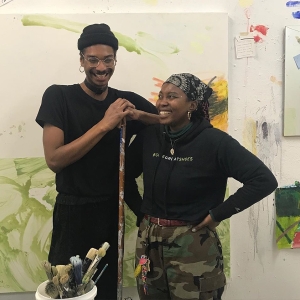 Two students stand and laugh together in the painting studio