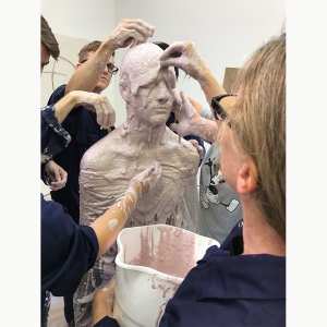 Sculpture students work together to put a wet clay mixture on a form