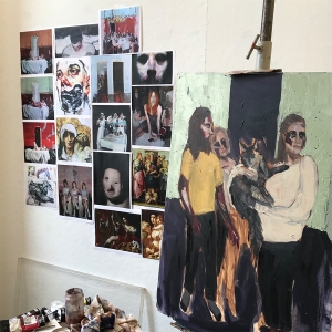 A student's studio with pictures taped to the wall and a work-in-progress on an art easel.