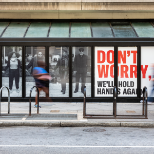 An image of a billboard with people holding hands that says "don't worry, we'll hold hands again" in red typeface.