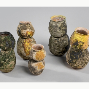 A set of green, brown and yellow stoneware that resembles vases with two circular forms stacked on top of each other