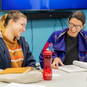 Two students sit at a table and laugh while reading a script during a Screenwriting class