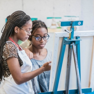 A Painting student and teacher review work on an easel
