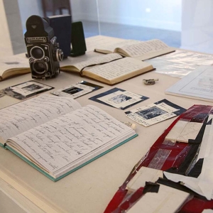 Detail view from installation of Joel-peter Witkin: From The Studio at Catherine Edelman Gallery. Photography equipment, scraps of paper, open notebooks and photographs with handwritten notes are displayed on a table in the gallery space.