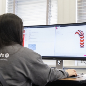 A student sits at a widescreen monitor with a worm-like shape on one side of the screen.