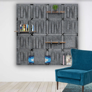 A rendering of an object on the wall of a room with a chair to showcase the scale of the object. The object is gray, possibly made out of a woolly material, with various slits/flaps placed in a minimal grid. There are wooden planks displayed as shelves, woven into the flaps, that are supporting books and a plant toward the top of the object. At the bottom, what looks like a rolled-up blanket is tucked in a flap, and magazines are behind the chair.