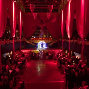 interior of solmssen court decorated in a moulin rouge theme. large drapes hang along the three stories of pillars, highlighted with crimson light. 