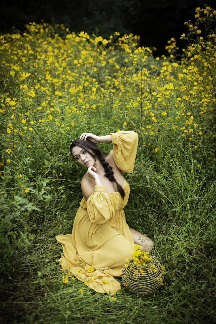 A female in a yellow dress sits in a field of yellow flowers.